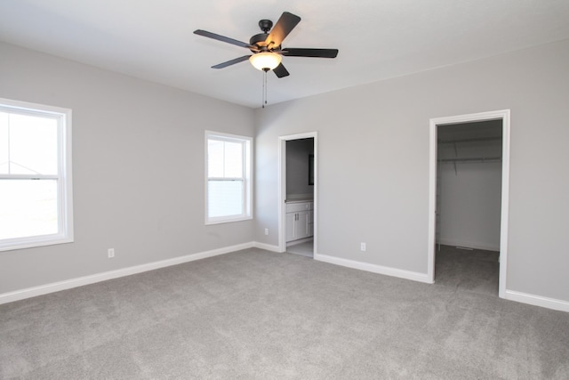 unfurnished bedroom with a closet, ceiling fan, a spacious closet, ensuite bath, and light colored carpet