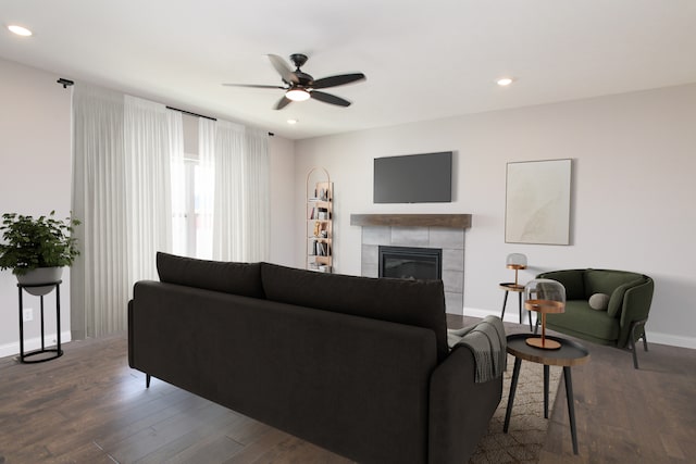 living room with a tiled fireplace, ceiling fan, and dark wood-type flooring