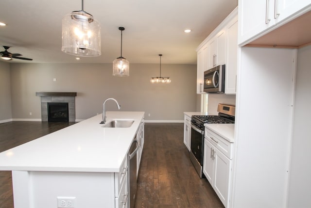 kitchen featuring appliances with stainless steel finishes, dark wood-type flooring, an island with sink, ceiling fan with notable chandelier, and sink