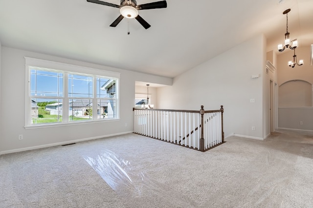 carpeted empty room featuring lofted ceiling, ceiling fan with notable chandelier, visible vents, and baseboards