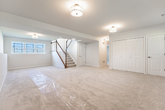 basement with light colored carpet, visible vents, baseboards, and stairs