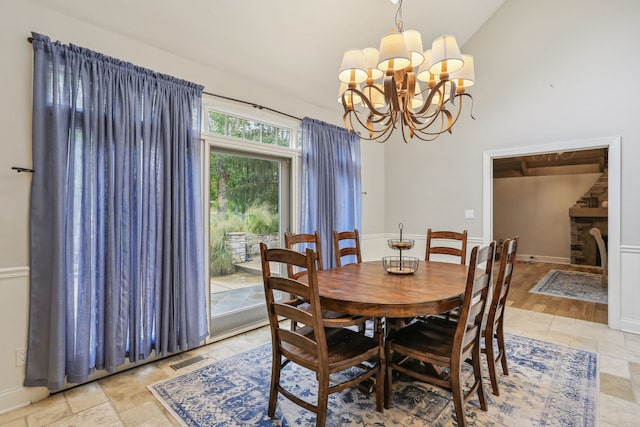 dining space with light tile floors, a notable chandelier, lofted ceiling, and a stone fireplace