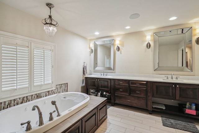 bathroom featuring an inviting chandelier, double vanity, and tiled bath