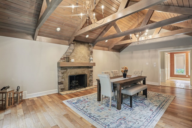 dining room featuring wood ceiling, a chandelier, light hardwood / wood-style flooring, lofted ceiling with beams, and a stone fireplace