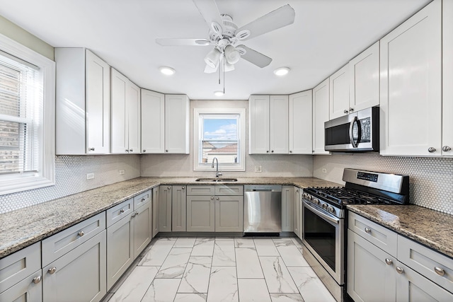 kitchen with appliances with stainless steel finishes, light stone counters, ceiling fan, sink, and light tile flooring