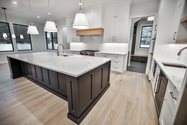 kitchen featuring light wood-type flooring, tasteful backsplash, light stone counters, sink, and white cabinets