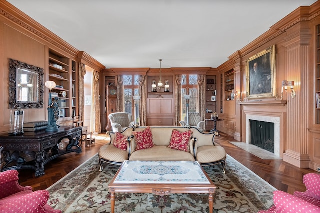 living room featuring built in shelves, a high end fireplace, a chandelier, crown molding, and dark parquet floors