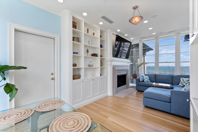 living room featuring ornamental molding, light hardwood / wood-style flooring, and built in shelves