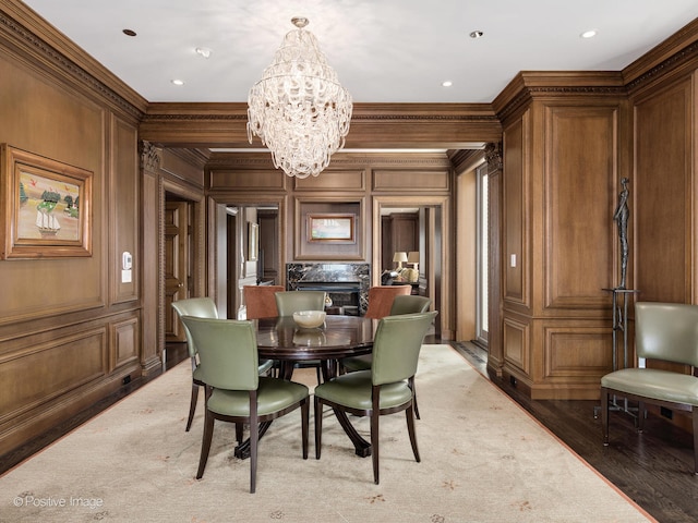 dining room featuring wooden walls, ornamental molding, hardwood / wood-style floors, an inviting chandelier, and a fireplace