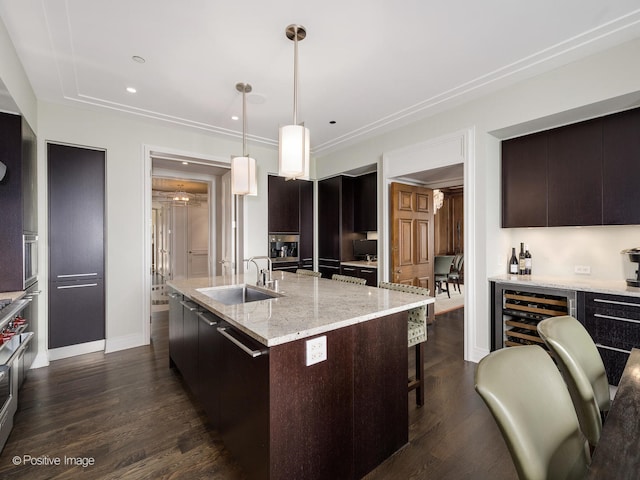 kitchen with beverage cooler, hanging light fixtures, a kitchen island with sink, dark wood-type flooring, and sink