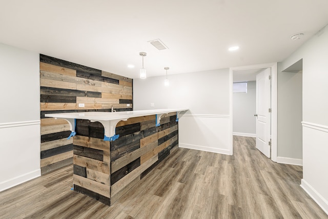 bar featuring light wood-type flooring, hanging light fixtures, and wood walls