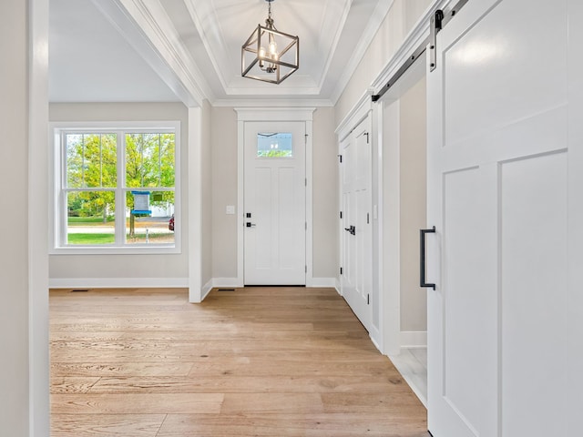 foyer entrance featuring a barn door, ornamental molding, a chandelier, and light wood-type flooring