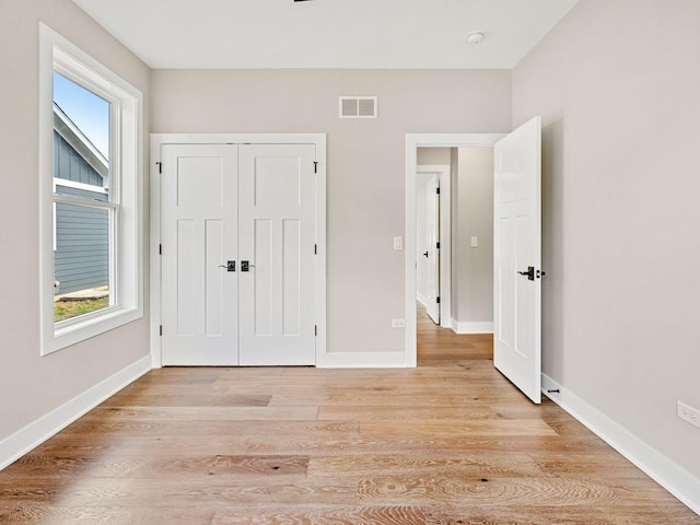 unfurnished bedroom featuring light wood-type flooring, multiple windows, and a closet