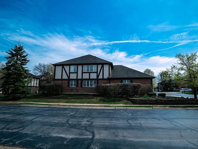 tudor home featuring stucco siding, uncovered parking, and brick siding