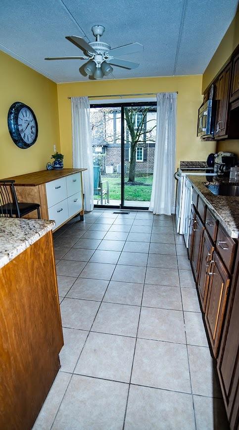 kitchen featuring a textured ceiling, stainless steel appliances, light tile patterned floors, and a ceiling fan