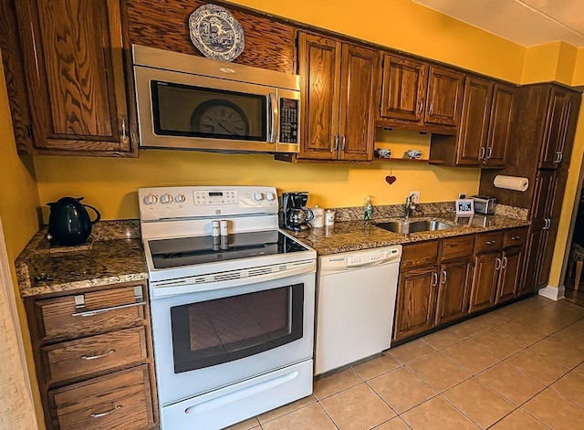 kitchen with dark stone countertops, light tile patterned floors, white appliances, and a sink