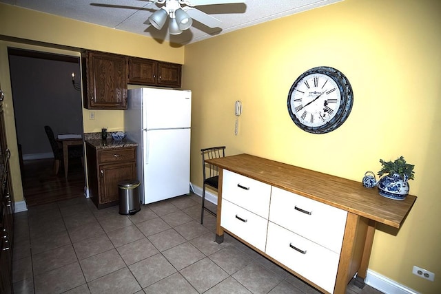 kitchen with freestanding refrigerator, dark tile patterned floors, dark brown cabinets, baseboards, and a ceiling fan