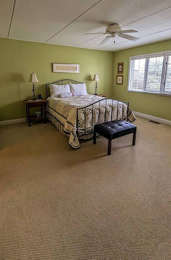 carpeted bedroom with baseboards, visible vents, ceiling fan, and a textured ceiling