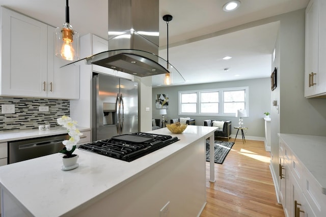 kitchen with hanging light fixtures, white cabinetry, appliances with stainless steel finishes, light wood-type flooring, and island exhaust hood