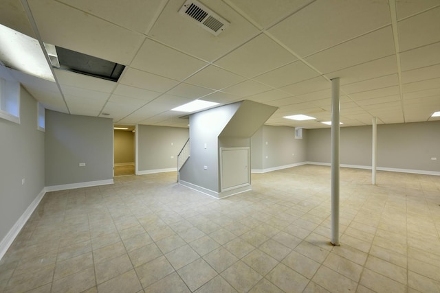 basement with a paneled ceiling and light tile floors