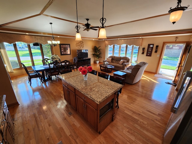 interior space with a kitchen bar, a kitchen island, light stone counters, light wood-type flooring, and hanging light fixtures