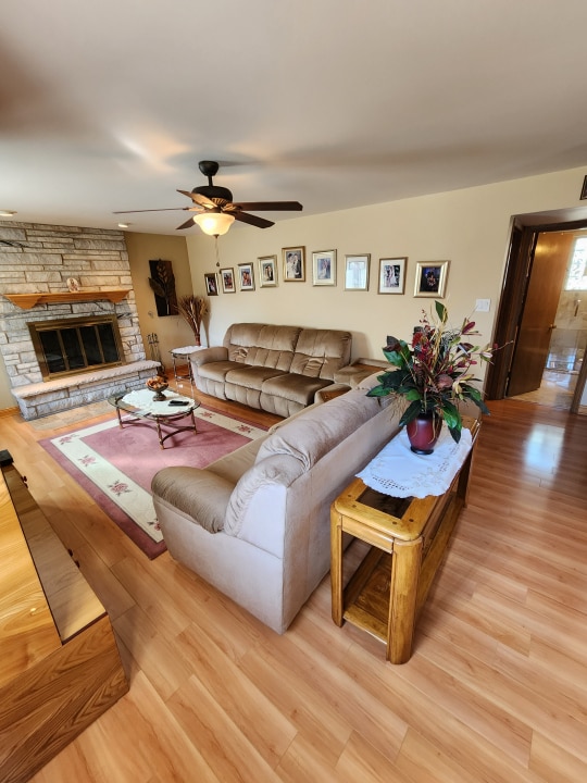 living room featuring ceiling fan, light wood-type flooring, and a fireplace