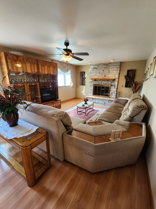 living room with light hardwood / wood-style flooring, ceiling fan, and a stone fireplace