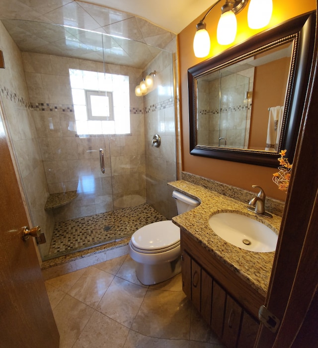 bathroom with tile floors, toilet, vanity, and a shower with door