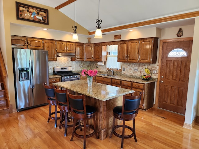 kitchen with appliances with stainless steel finishes, light wood-type flooring, a kitchen bar, vaulted ceiling, and sink