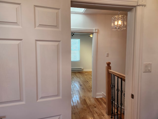 corridor with a skylight, a notable chandelier, light wood-type flooring, and baseboard heating