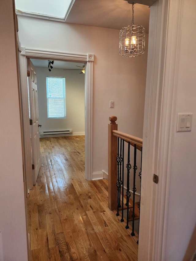 corridor featuring a baseboard radiator, a notable chandelier, light hardwood / wood-style flooring, and a skylight