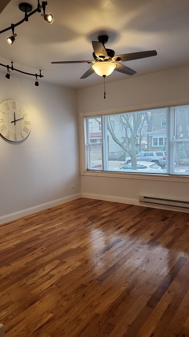 empty room with track lighting, ceiling fan, dark hardwood / wood-style floors, and a baseboard heating unit