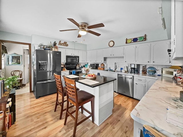 kitchen featuring ceiling fan, light hardwood / wood-style flooring, a breakfast bar, and black appliances