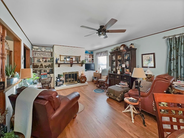 living room featuring ceiling fan, light hardwood / wood-style flooring, a fireplace, brick wall, and crown molding