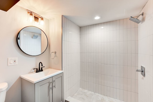 bathroom with toilet, a tile shower, and vanity