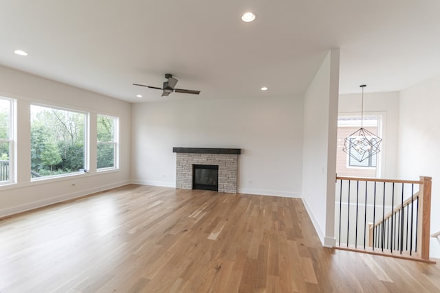 unfurnished living room featuring a stone fireplace, ceiling fan with notable chandelier, and light wood-type flooring