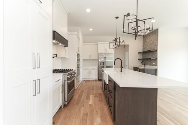 kitchen with light hardwood / wood-style flooring, premium appliances, a center island with sink, tasteful backsplash, and white cabinetry