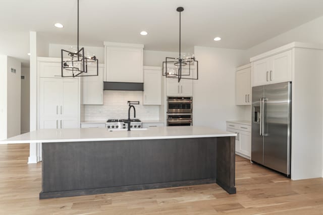 kitchen with appliances with stainless steel finishes, a kitchen island with sink, white cabinetry, and light hardwood / wood-style floors