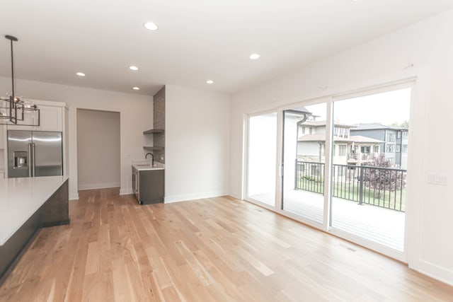 unfurnished living room featuring a notable chandelier, light hardwood / wood-style flooring, sink, and plenty of natural light