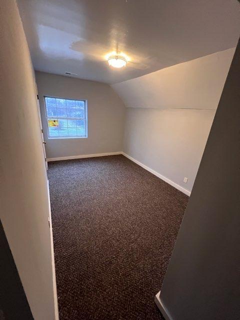 bonus room with dark carpet and lofted ceiling