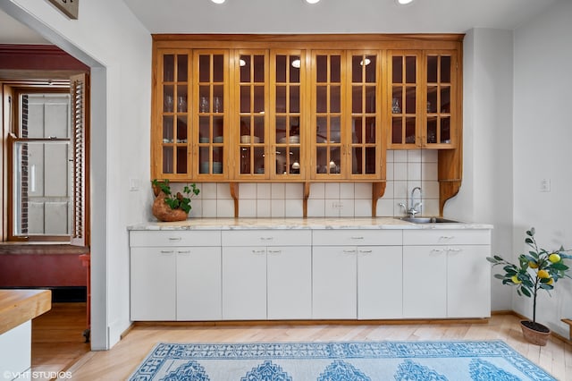 interior space with backsplash, sink, light wood-type flooring, white cabinets, and light stone counters