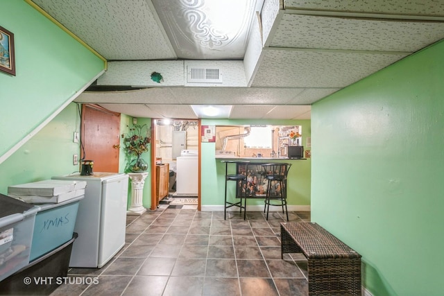 basement with bar, washer / clothes dryer, a paneled ceiling, and tile patterned floors