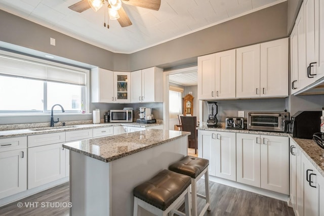 kitchen featuring a kitchen bar, sink, light stone counters, a kitchen island, and white cabinets