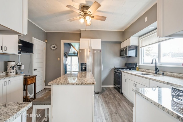 kitchen with sink, white cabinetry, appliances with stainless steel finishes, a kitchen breakfast bar, and light stone countertops