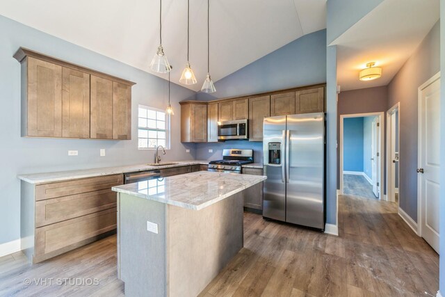 kitchen featuring stainless steel appliances, light stone countertops, hardwood / wood-style floors, lofted ceiling, and a center island