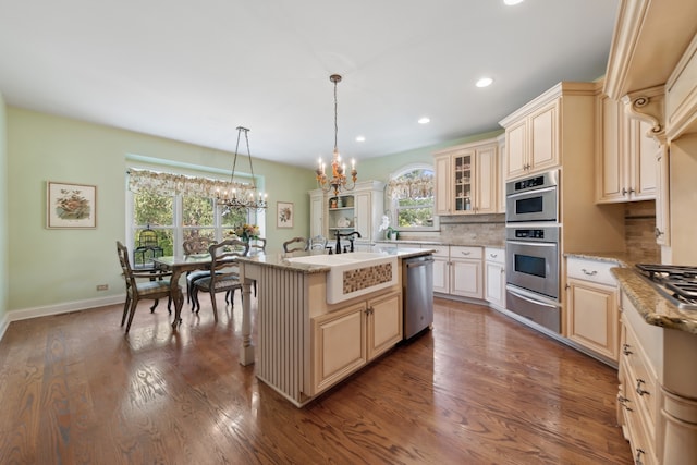 kitchen with appliances with stainless steel finishes, dark hardwood / wood-style floors, backsplash, and an island with sink