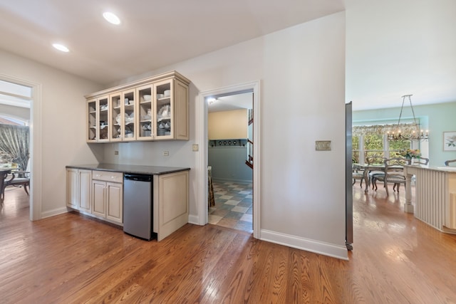 kitchen with stainless steel dishwasher, pendant lighting, cream cabinetry, light wood-type flooring, and an inviting chandelier