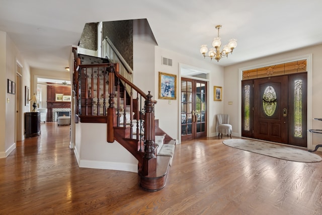 foyer featuring dark hardwood / wood-style flooring, a notable chandelier, a fireplace, and french doors