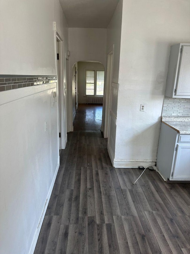 hallway with arched walkways, dark wood-type flooring, and radiator