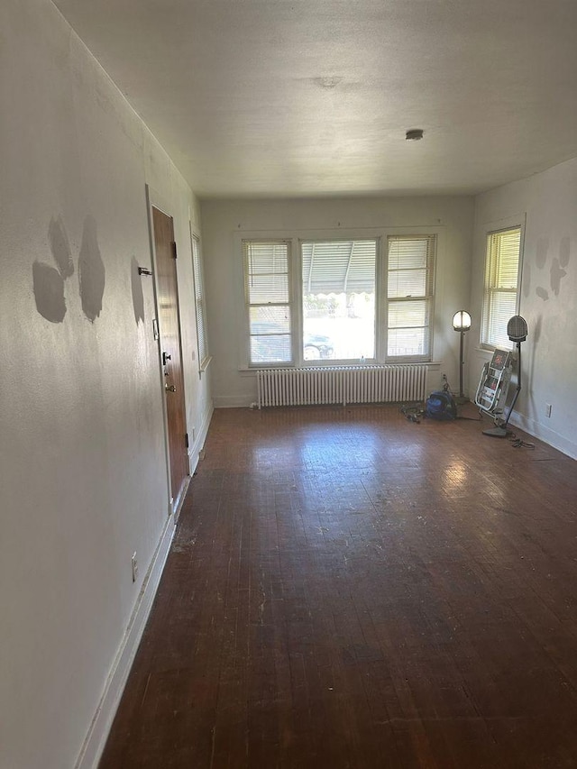 empty room with radiator heating unit, wood-type flooring, and baseboards